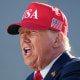 Donald Trump speaks, wearing a red hat that reads "USA" in white text