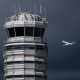 An airplane flies near a control tower on a dark cloudy day