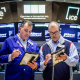 Two people look at tablets on the floor of the New York Stock Exchange building, tv screens behind them