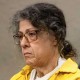 Susan Lorincz sits in court, a police officer sits behind her