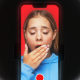 A girl yawning on a phone screen with a record button, surrounded by a ring light.