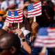 Images: New US citizens use handheld fans to take shade from the sun during a naturalization ceremony