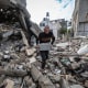 A person holds a cinderblock while walking on top of rubble outside