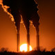 Silhouettes of large billowing smoke coming out of smoke stacks as the sun sets