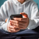 Close up of hands of teen boy in white sweater texting on phone.