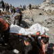 People carry a body wrapped in white tarp out from the rubble