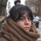Val Calderon stands outside wearing a large chunky brown scarf and coat, a tear begins to stream down her face