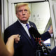 Donald Trump stands in a doorway aboard Air Force One as reporters crowd around him with microphones