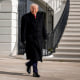 President Trump walks on the patio outside the White House on a sunny day.