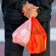 A pedestrian carries plastic shopping bags.