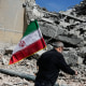 A man carries an Iranian flag to place on the rubble