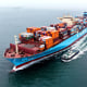 A cargo ship loaded with foreign trade containers sails on the water next to smaller boats