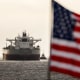 An American flag appears in soft-focus in the foreground. Behind it several ships float in the water.