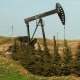 An oil pump jack rises above the horizon against a clear blue sky.