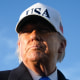 Donald Trump wears a white baseball cap with the acronym USA on the front