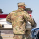 Army members carry a casket across an aircraft tarmac as Donald Trump and company stand to watch while saluting