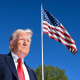 Donald Trump stands outside near an American flag flying on a flagpole above him