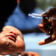 A hand holds a vaccine administer near a infant's face