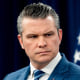 Pete Hegseth stands near an American flag behind him
