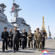 Kim Jong Un walking on a cement platform surrounded by other men in uniform.