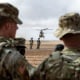 Soldiers look at a plan taking off in the distance outside