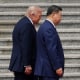 Donald Trump and Xi Jinping walk side-by-side in front of a concrete staircase.