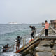Three men wearing diving equipment make their way up a staircase from the water. 
