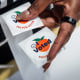 A hand holds an "I Voted" sticker with a peach on it