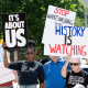 People hold signs that say "Black Voter Matter", "It's About Us", and "History Is Watching" while standing outside