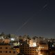 Streaks from a missile in the air over rooftops at night.