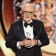 John Lithgow holding an Emmy, dressed in a tuxedo.