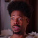 Marlon Wayans sits on a couch in a living room surrounded by foam with tears streaming down his face