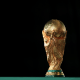 The gold world cup trophy is displayed against a black backdrop.