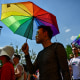 A person holds an umbrella in the colors of a Pride flag.