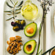 Still life of foods like olives, canola oil, mackerels, flaxseeds, avocado, and walnuts.