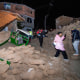 People walk amid debris outside near houses, photo taken with flash at night