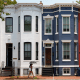 A woman with an umbrella walks past red, white and blue painted row houses.