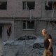 A man walks past while a man stands on a destroyed car following an air attack.