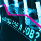 Photo illustration of a row of graduates holding diplomas with an arrow pointing down. Text that reads "Looking for a job?"
