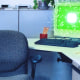 An empty office chair and a computer screen illuminated with digital, AI chip texture in a cubicle.
