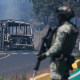 A soldier stands guard by a charred vehicle.
