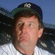 Tommy John sits on the baseball field in uniform, holding a catcher's mitt