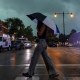 A woman crosses the street while holding an umbrella as a rain storm appears to occur. 