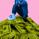 A woman (colorized in blue) who is crouched with her hands covering her face, seated atop a large pile of dollar bills (colorized in lime green), 20s, 10s, 5s and 1s can be seen in the mountainous pile, all against a pink background