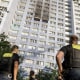 two police officers look up at black smoke coming from the middle of a high-rise apartment building.