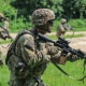 Luke Lem in his army uniform carries a gun while walking in a field