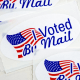 Stickers that read "I Voted By Mail" sit on a table