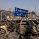 A burned car sitting in the midst of further wreckage after an explosion.
