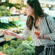 Woman holding carrots in one hand and looking for other produce in the local grocery store.