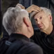 A man examines his hairline in the mirror.